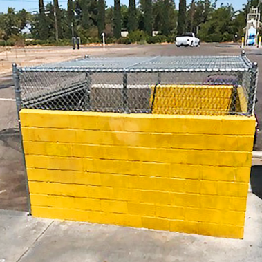 A bright yellow brick cage protects a property, featuring a sturdy chain link gate for access.