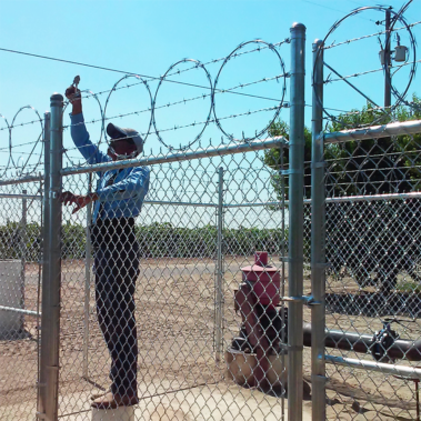 A man stands on a fence topped with razor wire, highlighting precision in installation