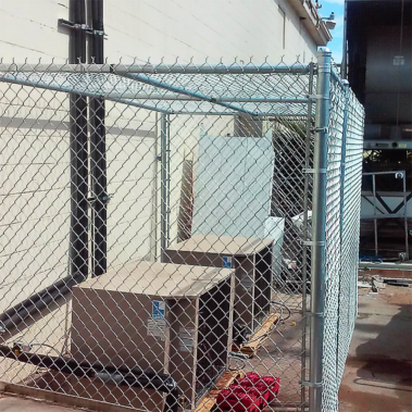 A chain link fence enclosing two air conditioning units, showcasing a blend of utility and security in an outdoor setting.
