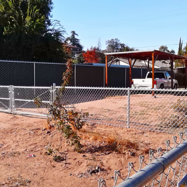 A chain link fence stands tall in a dusty lot, marking the boundary of an outdoor parking garage