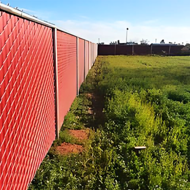 A red fence stands prominently in the center of a vast green field under a clear blue sky.