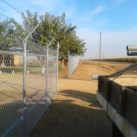 A truck is parked beside a fence along a dirt road, surrounded by a natural landscape.