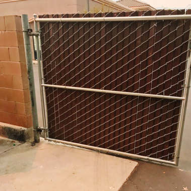 A sturdy metal gate stands alongside a brown wooden fence, creating a secure and rustic boundary.